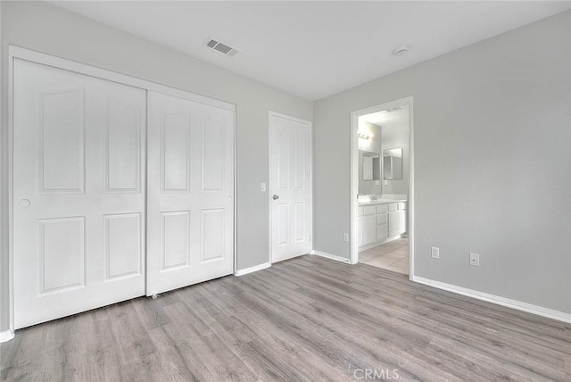 unfurnished bedroom featuring wood finished floors, visible vents, baseboards, a closet, and ensuite bath