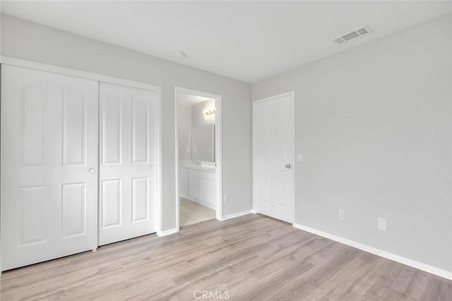 unfurnished bedroom featuring a closet, visible vents, light wood-style floors, connected bathroom, and baseboards