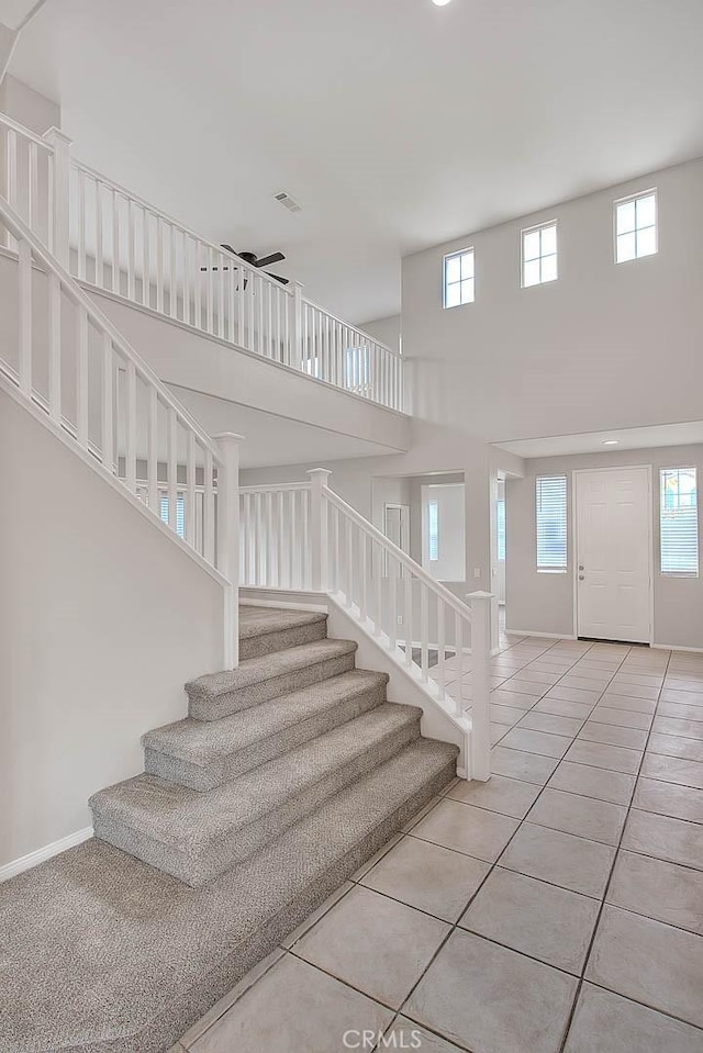 staircase with tile patterned flooring, visible vents, a towering ceiling, and baseboards