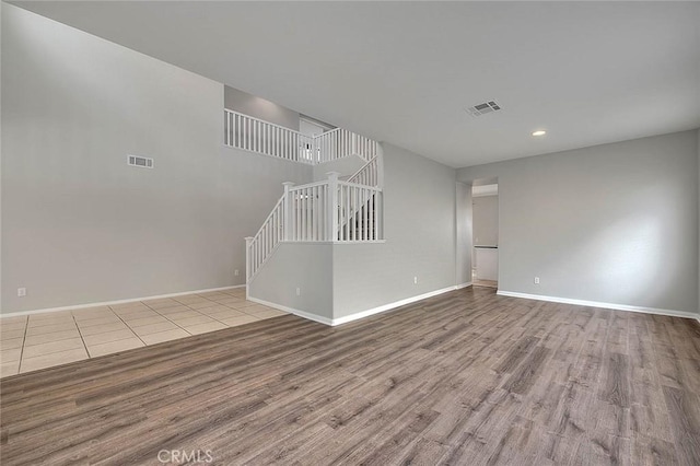 unfurnished living room with stairs, wood finished floors, visible vents, and baseboards