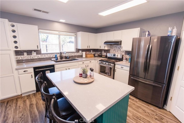 kitchen featuring visible vents, white cabinets, stainless steel appliances, under cabinet range hood, and a sink