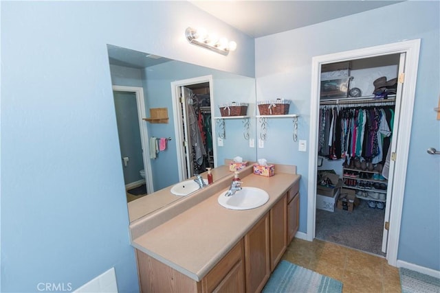 bathroom with toilet, baseboards, a walk in closet, and vanity