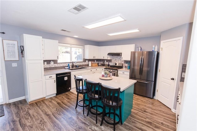 kitchen featuring stainless steel appliances, visible vents, a sink, under cabinet range hood, and a kitchen bar