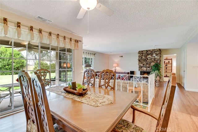 dining area featuring light wood-style flooring, visible vents, a textured ceiling, and a stone fireplace