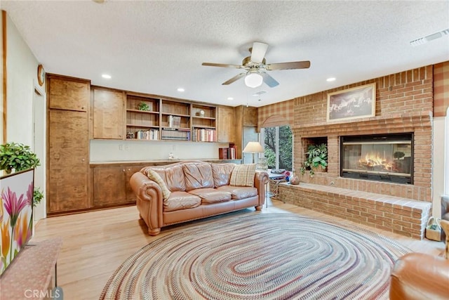 living room featuring a brick fireplace, light wood-style flooring, visible vents, and a textured ceiling