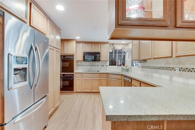 kitchen featuring light wood-style flooring, light stone counters, backsplash, black appliances, and a sink