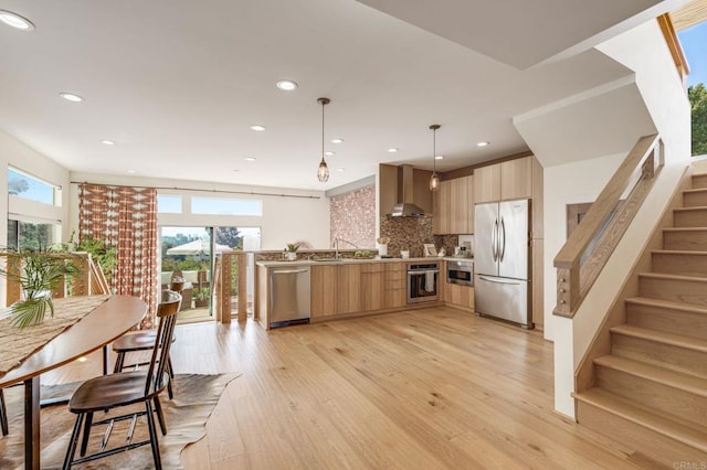 kitchen with light wood-style flooring, modern cabinets, appliances with stainless steel finishes, light brown cabinetry, and wall chimney range hood