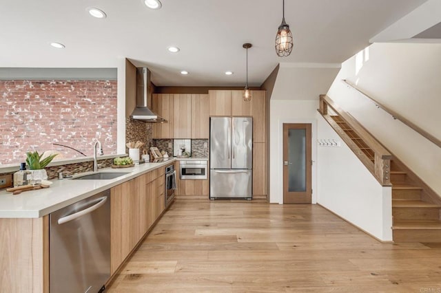 kitchen with appliances with stainless steel finishes, a sink, wall chimney range hood, and modern cabinets