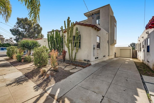 view of property exterior featuring stucco siding, fence, a garage, driveway, and an outdoor structure