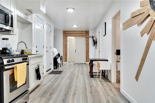 kitchen with appliances with stainless steel finishes, light wood-type flooring, white cabinets, and baseboards