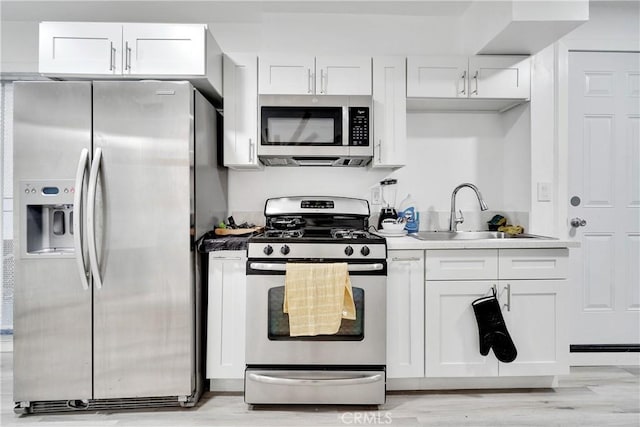 kitchen featuring stainless steel appliances, a sink, white cabinetry, and light wood-style floors