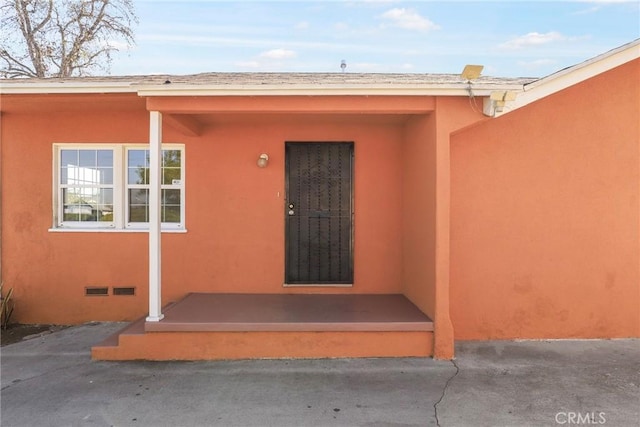 view of exterior entry with crawl space and stucco siding