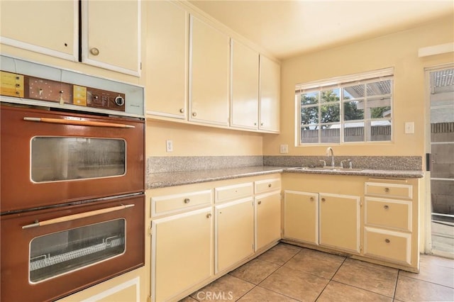 kitchen with light tile patterned floors, double wall oven, light countertops, cream cabinetry, and a sink