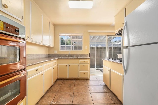 kitchen featuring light tile patterned floors, freestanding refrigerator, light countertops, stainless steel gas stovetop, and a sink