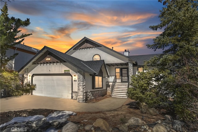 view of front of house featuring roof with shingles, a chimney, a garage, stone siding, and driveway