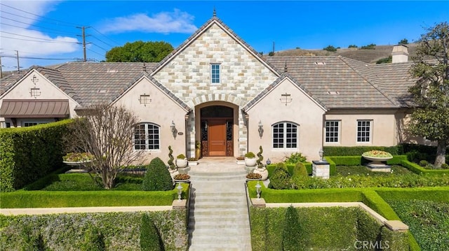 view of front of house with a front yard, stone siding, a chimney, and stucco siding