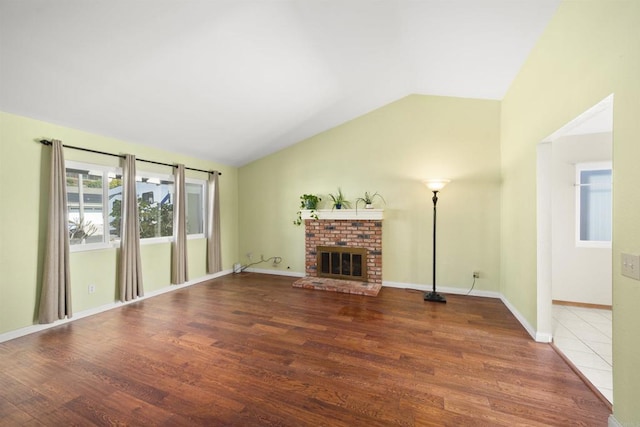 unfurnished living room with lofted ceiling, a fireplace, baseboards, and wood finished floors