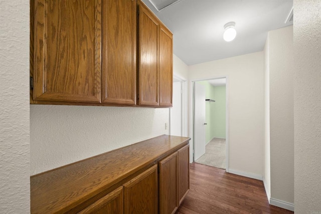 corridor featuring a textured wall, dark wood-type flooring, and baseboards