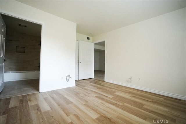 unfurnished bedroom featuring visible vents, connected bathroom, baseboards, and wood finished floors