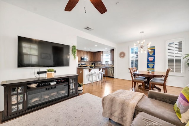 living area with recessed lighting, light wood-style flooring, visible vents, and ceiling fan with notable chandelier