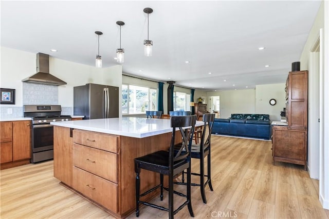 kitchen featuring light wood-style floors, a center island, light countertops, stainless steel appliances, and wall chimney range hood