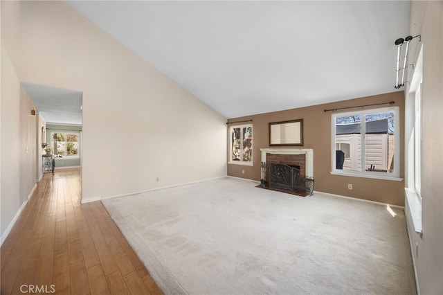 unfurnished living room featuring high vaulted ceiling, a brick fireplace, carpet floors, and baseboards