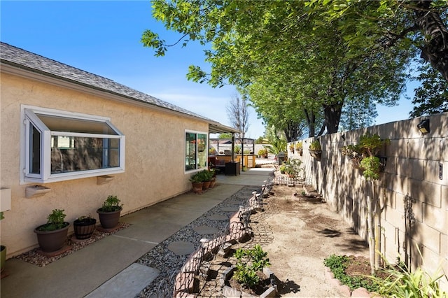 view of side of home with a patio area, a fenced backyard, a shingled roof, and stucco siding