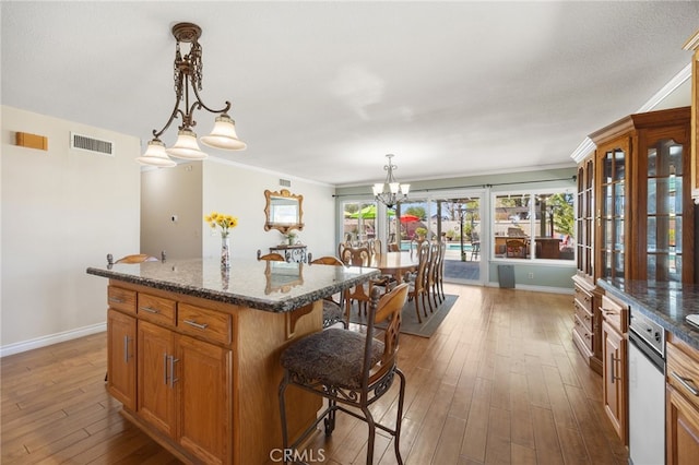 kitchen with a breakfast bar area, a kitchen island, visible vents, brown cabinets, and wood-type flooring