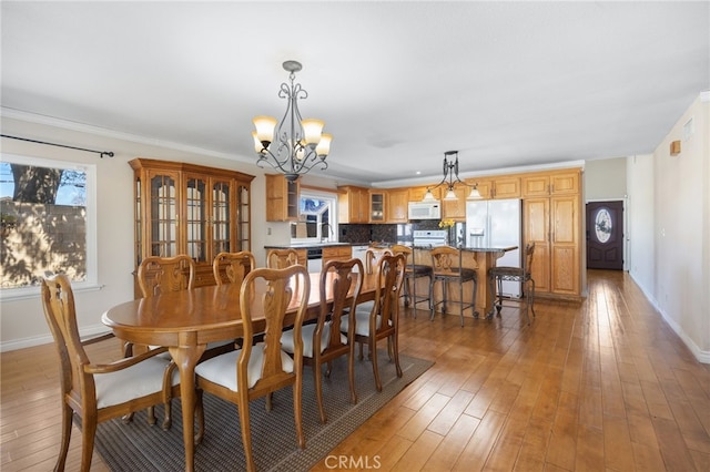 dining room with a chandelier, baseboards, a healthy amount of sunlight, and light wood finished floors