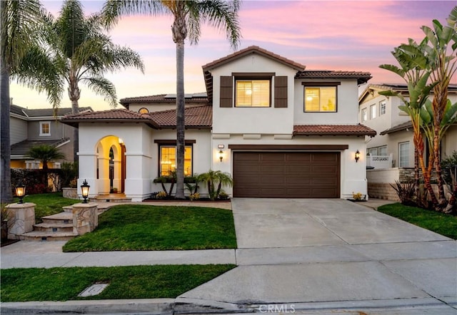 mediterranean / spanish-style house with concrete driveway, a tiled roof, an attached garage, a yard, and stucco siding