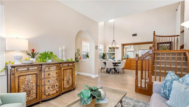 living room featuring baseboards, stairs, light wood-type flooring, high vaulted ceiling, and a notable chandelier