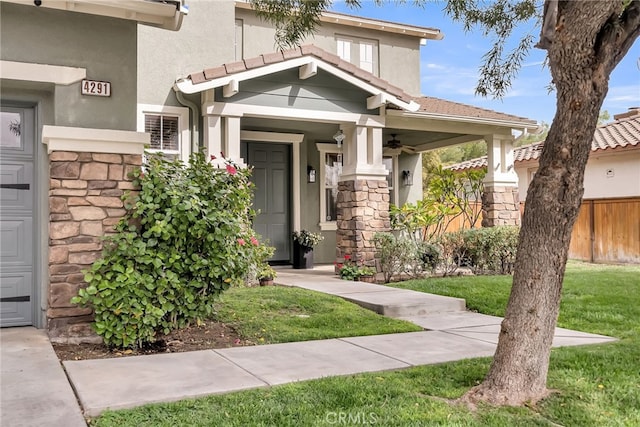 view of front of property with stucco siding, a ceiling fan, fence, a garage, and stone siding