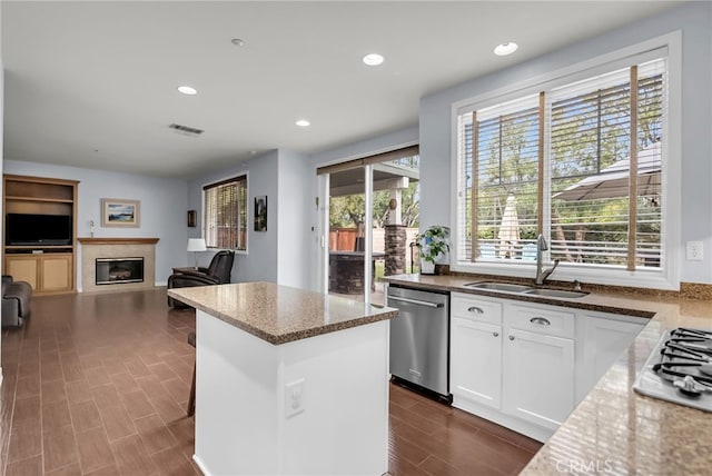 kitchen with appliances with stainless steel finishes, a glass covered fireplace, wood tiled floor, a sink, and a kitchen island