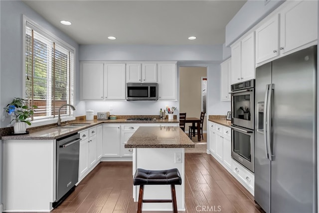 kitchen with stainless steel appliances, dark wood-type flooring, white cabinetry, a sink, and dark stone countertops