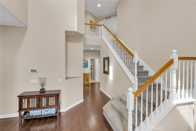 stairway with recessed lighting, wood finished floors, a towering ceiling, and baseboards