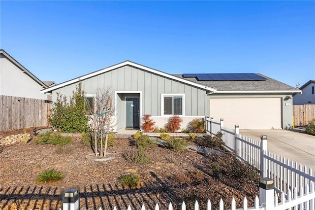 single story home with solar panels, concrete driveway, an attached garage, fence, and board and batten siding