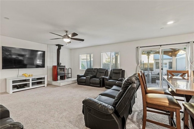 carpeted living area with a wood stove and ceiling fan