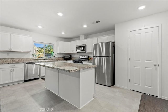 kitchen with visible vents, white cabinets, a kitchen island, light stone countertops, and stainless steel appliances