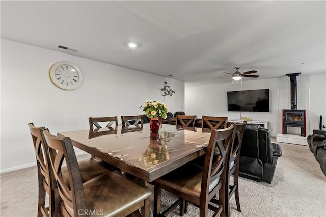 dining area featuring light carpet, baseboards, visible vents, a ceiling fan, and a wood stove