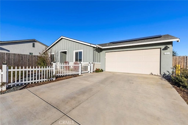 single story home featuring a fenced front yard, an attached garage, solar panels, concrete driveway, and board and batten siding