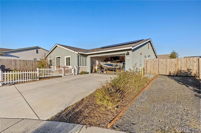 view of front of home with fence private yard, a garage, solar panels, driveway, and board and batten siding