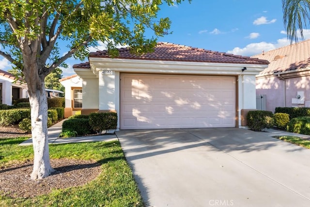 mediterranean / spanish house featuring concrete driveway, a tiled roof, an attached garage, and stucco siding