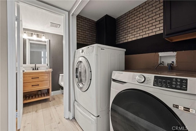 clothes washing area with light wood finished floors, cabinet space, visible vents, a sink, and washer and dryer