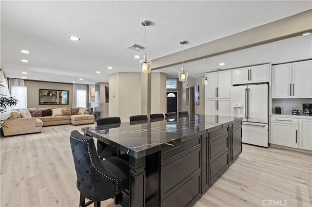 kitchen featuring high end white refrigerator, visible vents, a kitchen breakfast bar, light wood-style floors, and white cabinetry