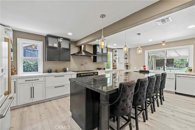 kitchen featuring white appliances, visible vents, light wood-style floors, wall chimney range hood, and a kitchen bar