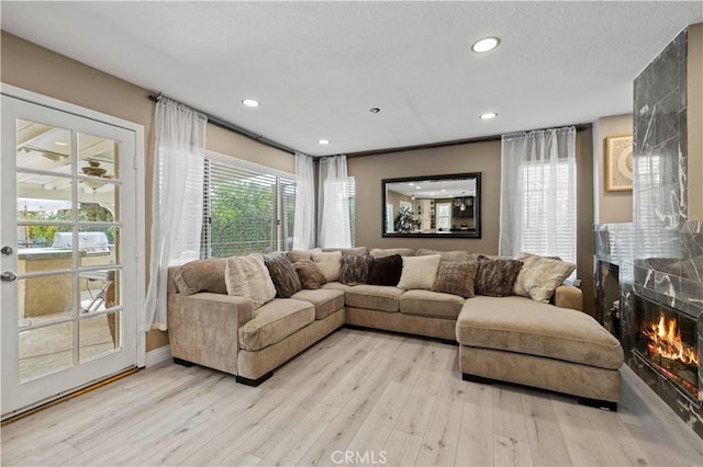 living room featuring recessed lighting, a healthy amount of sunlight, light wood finished floors, and a premium fireplace