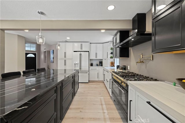 kitchen featuring light wood-style flooring, dark cabinets, wall chimney range hood, high end appliances, and dark stone countertops