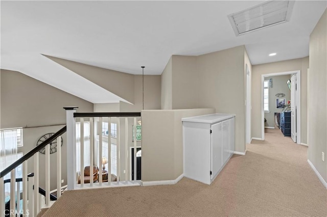 hallway with light carpet, baseboards, visible vents, and vaulted ceiling