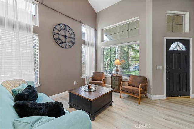 living room featuring light wood-style flooring, high vaulted ceiling, and baseboards