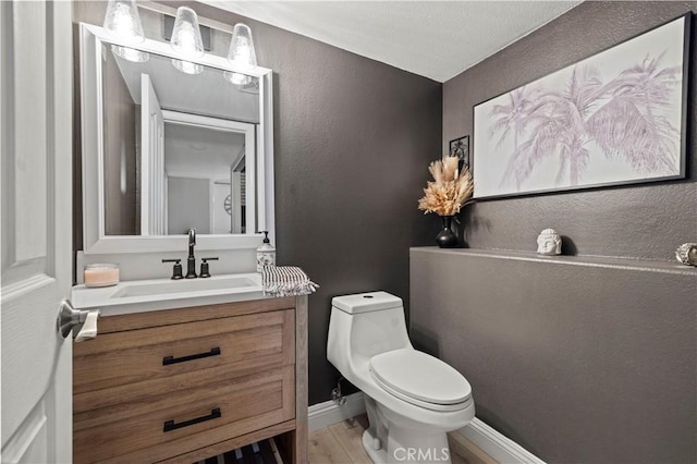 half bathroom featuring toilet, baseboards, wood finished floors, and vanity